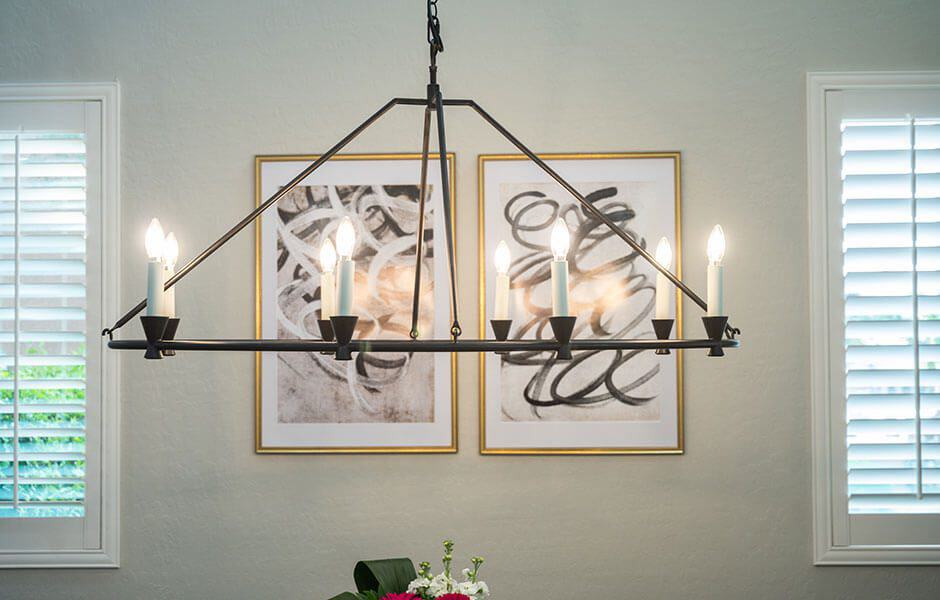 A chandelier with a metal frame and candle-style bulbs hanging above a dining table