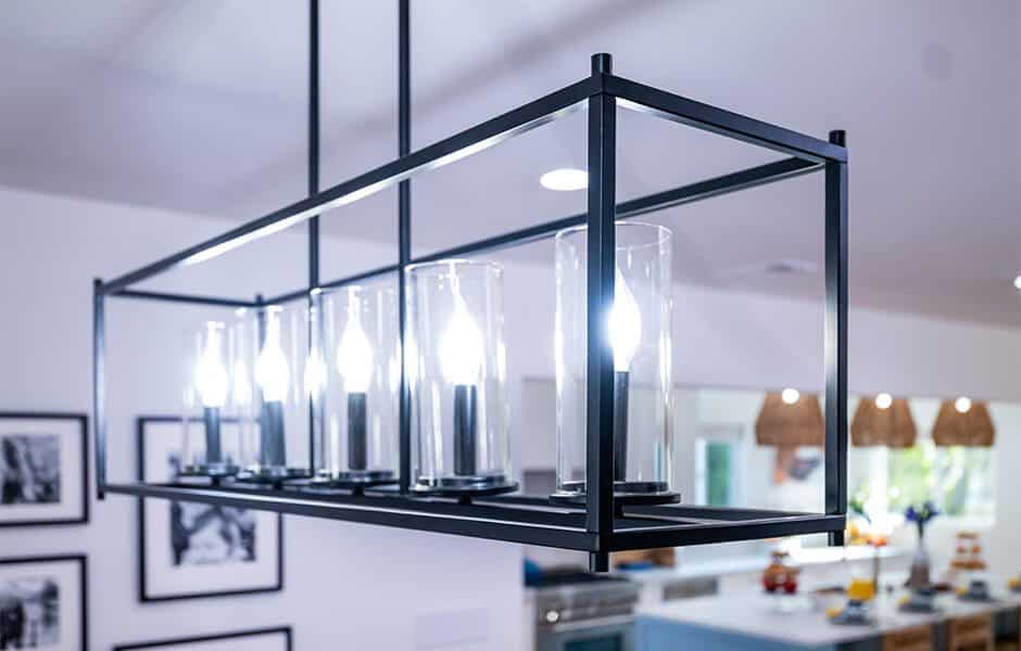 Modern rectangular chandelier with black metal frame and five glass-enclosed lights hanging in a bright room