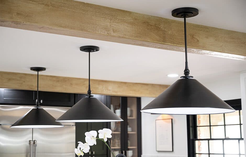 Black industrial pendant lights hanging from a wooden ceiling beam in a modern kitchen