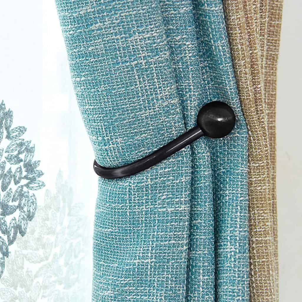 Blue textured curtain held back by a black metal hook against a sheer white and beige curtain