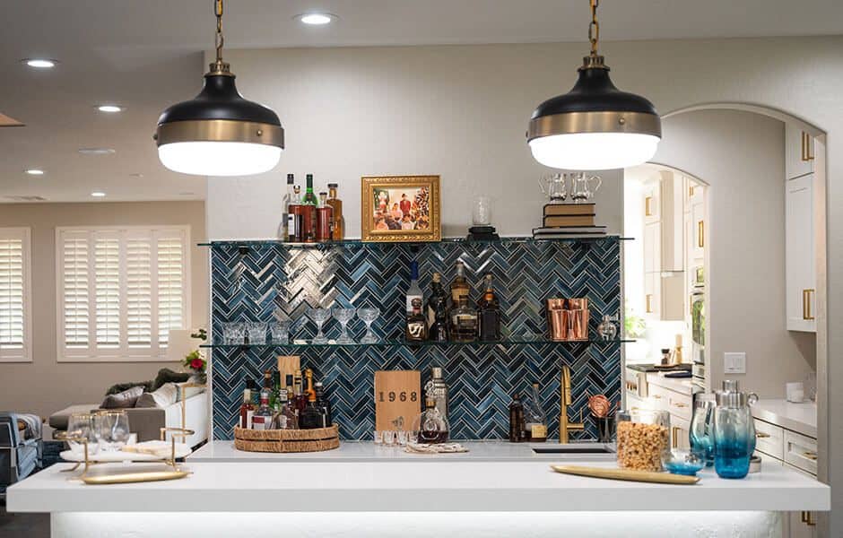 Stylish home bar with a blue herringbone backsplash, glass shelves, and pendant lighting