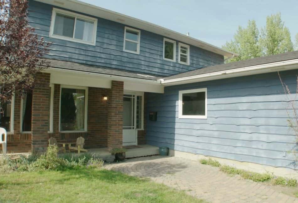 Two-story blue house with brick porch, paved driveway, and lawn