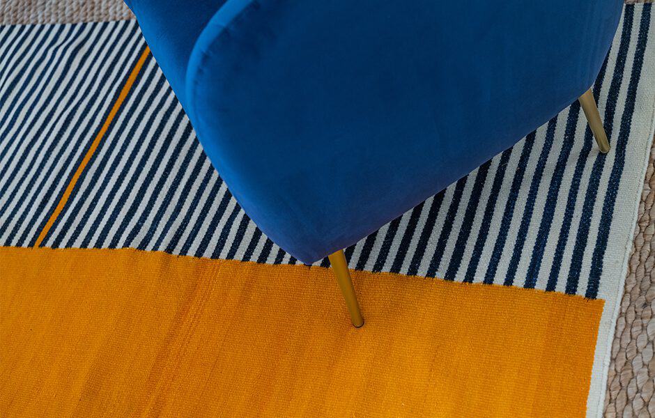 Bold striped rug in blue, white, and orange pairs with a blue chair and gold legs