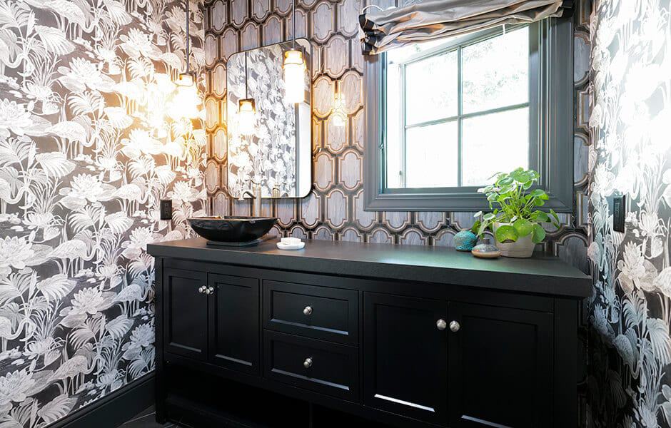 Black vanity with patterned wallpaper and a vessel sink in a bright bathroom