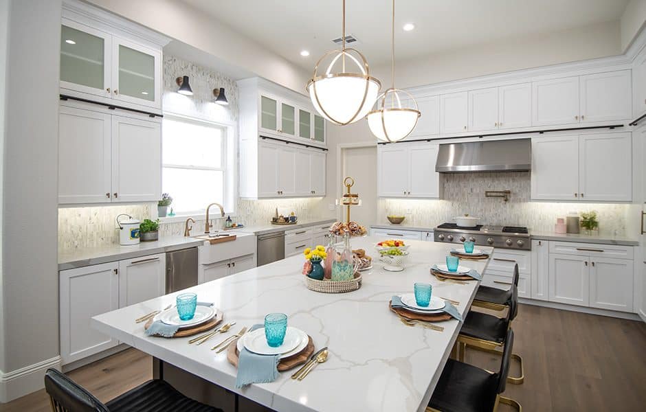 Spacious kitchen with white cabinets, quartz countertop, pendant lights, farmhouse sink, tiled backsplash, and island set for a meal