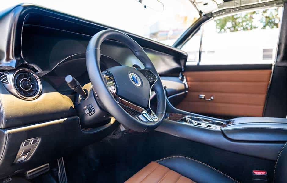 Luxury car interior with a black leather steering wheel, tan leather seats, and modern controls