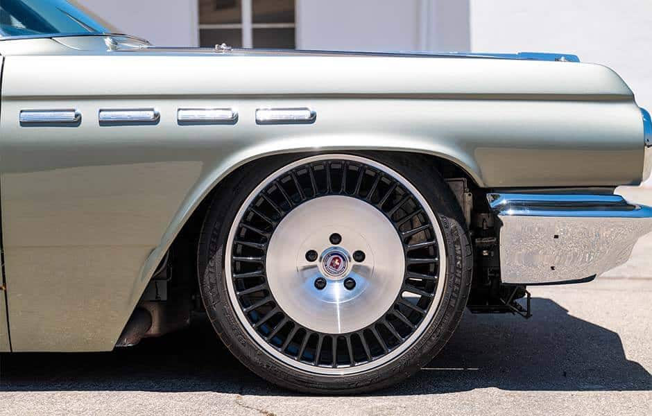 Close-up of a vintage car's front wheel and fender, featuring a polished custom rim and classic design details