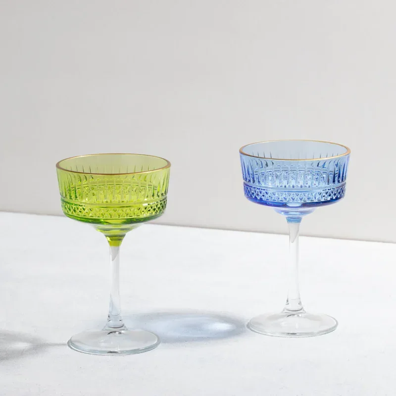 Green and blue crystal coupe glasses with intricate cut patterns and clear stems