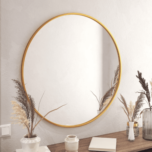 Round gold-framed mirror on a wall above a wooden surface, decorated with dried plants in vases and a notebook