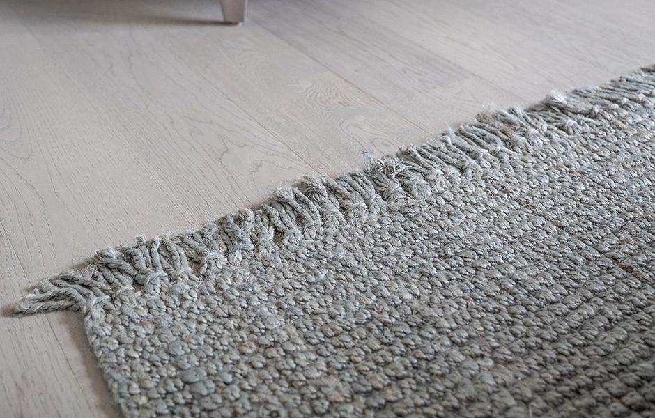 Close-up of textured gray rug with fringe detail on light hardwood flooring