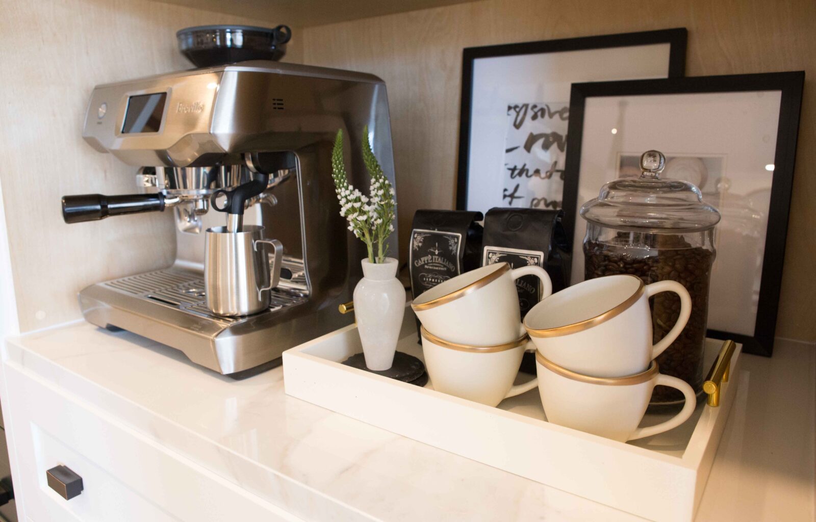Coffee station with an espresso machine, gold-rimmed cups, coffee beans, and decorative accents