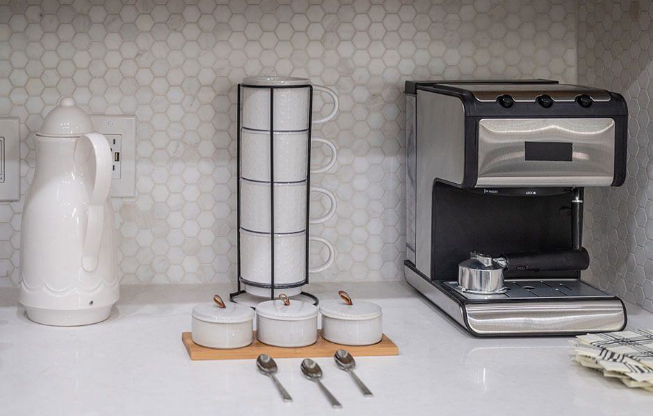 Kitchen coffee station with stainless steel espresso machine white cups and hexagon tile backsplash