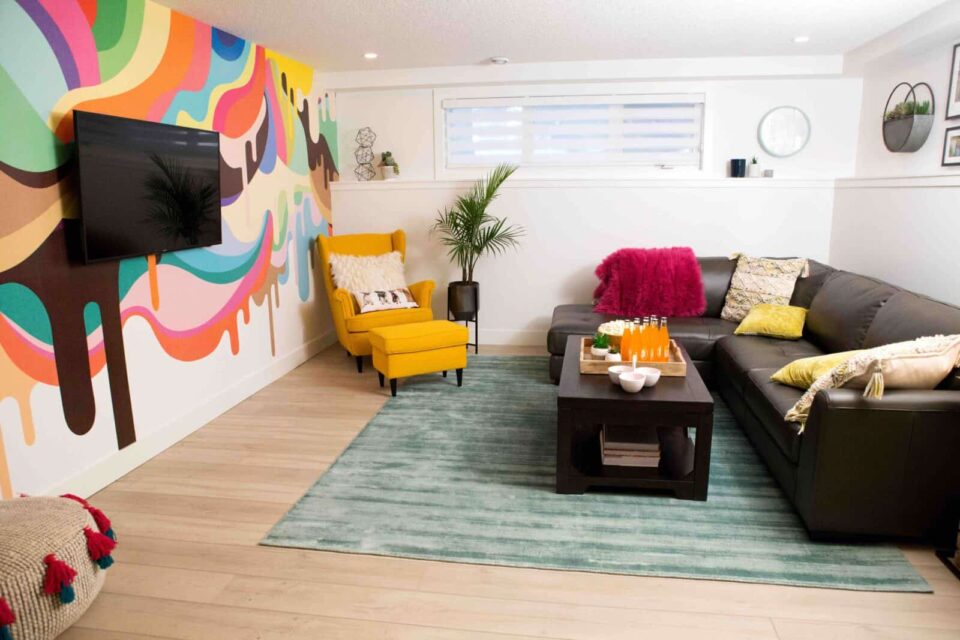 Colorful living room with a mural wall, yellow armchair, black sectional sofa, and a teal rug