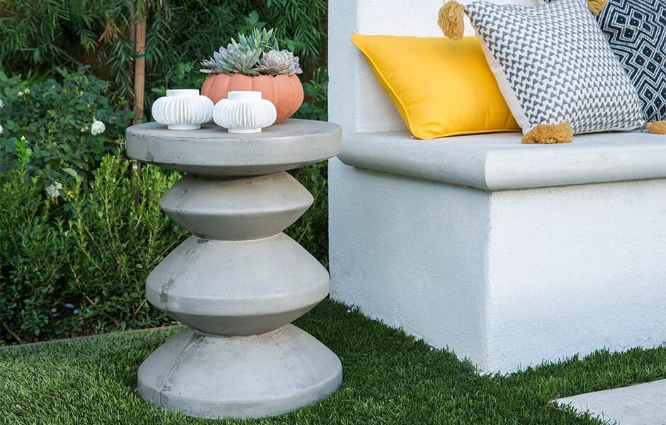 Outdoor seating with a concrete side table, vases, a succulent, and colorful pillows