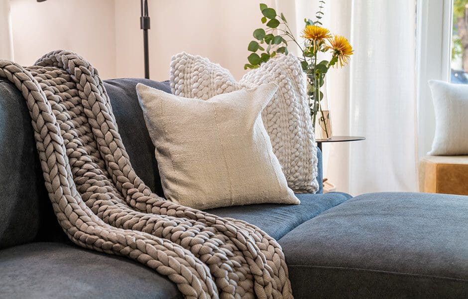 Living room corner with a blue sofa, knit blanket, and pillows
