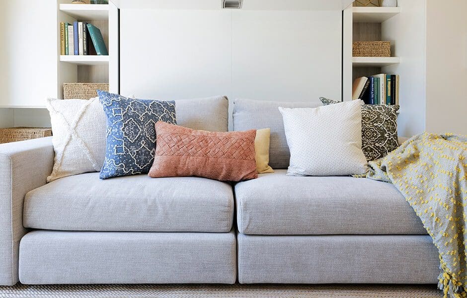 Light gray sofa with assorted decorative pillows in various colors and patterns, flanked by bookshelves