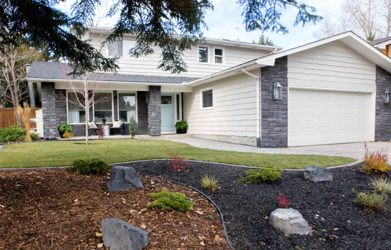 Two-story suburban house with stone accents, a white garage, and landscaped front yard