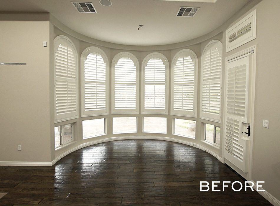 Room with curved windows, white shutters, dark wood floors, and beige walls