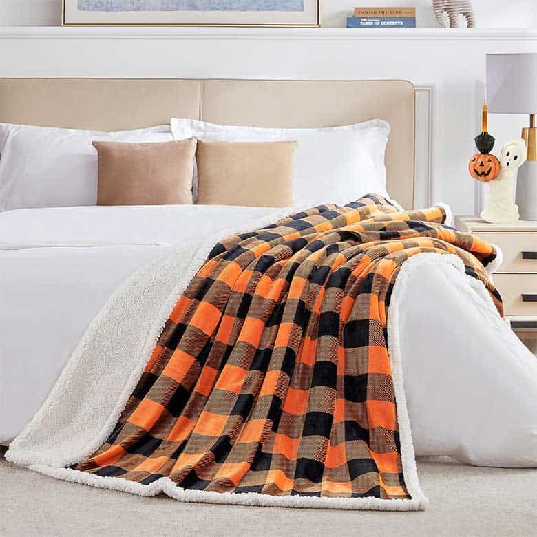 Orange and black plaid sherpa blanket draped over a white bed in a cozy, fall-themed bedroom