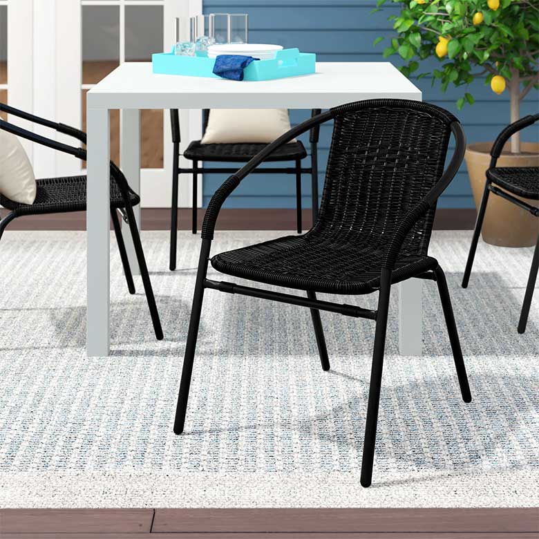 Black woven patio chair with curved arms, placed next to a white outdoor dining table