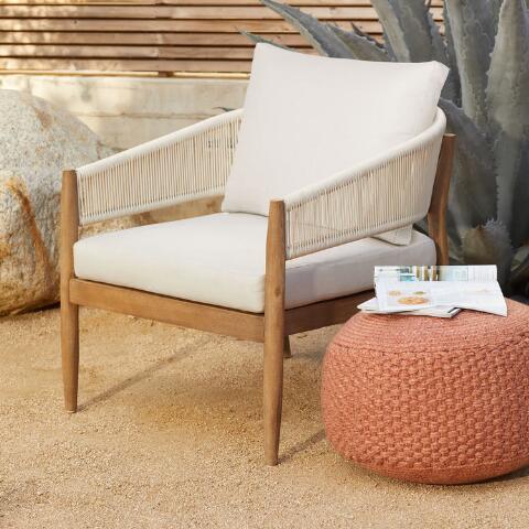 Outdoor lounge chair with wooden frame woven rope arms and cream cushions next to a textured ottoman