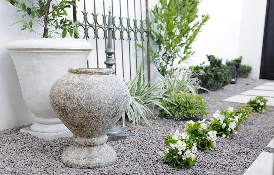 Garden with gravel ground cover, white planters, green shrubs, and a row of white flowers