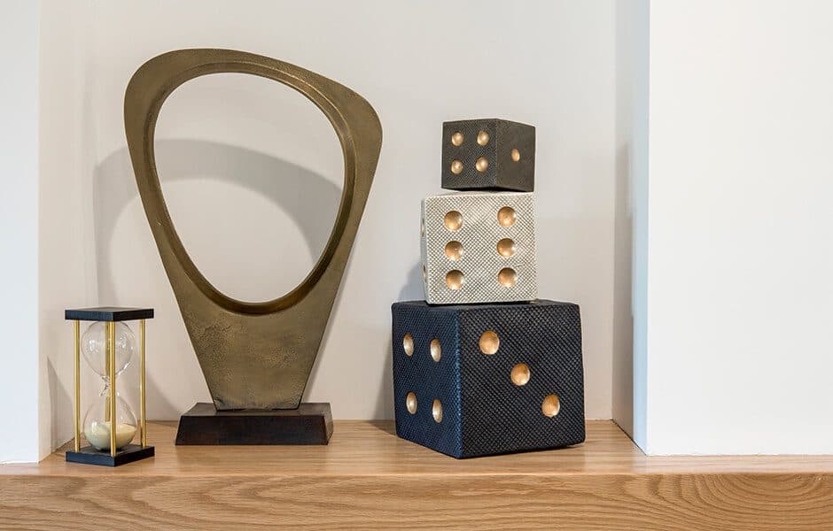 Decorative shelf with a gold hourglass, abstract bronze sculpture, and stacked textured dice ornaments