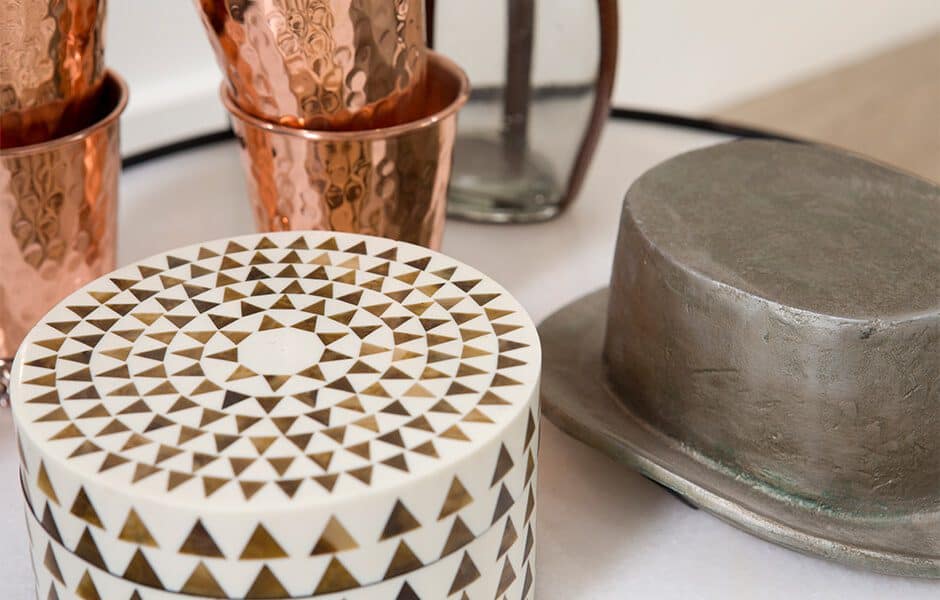 Decorative tabletop with copper cups, patterned round box, and a metallic hat sculpture