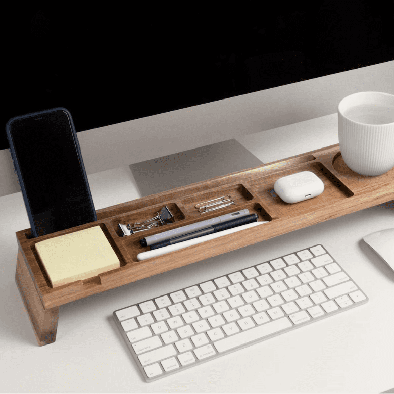 Wooden desk organizer holding a phone, pens, sticky notes, clips, AirPods, and a coffee cup