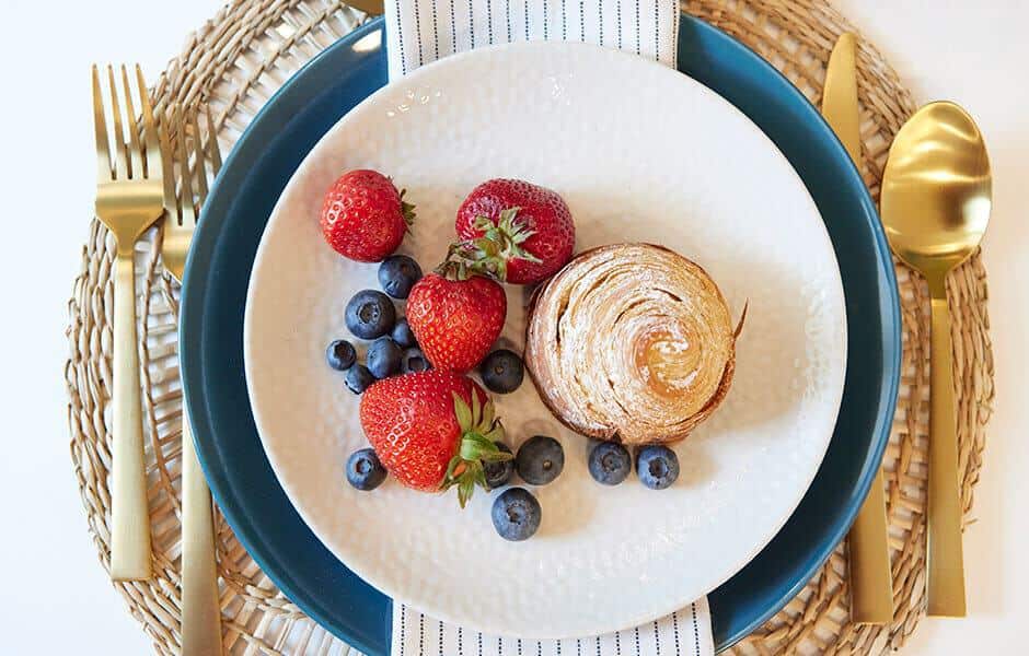 Elegant breakfast setting with fresh berries, a pastry, and gold flatware on a woven placemat