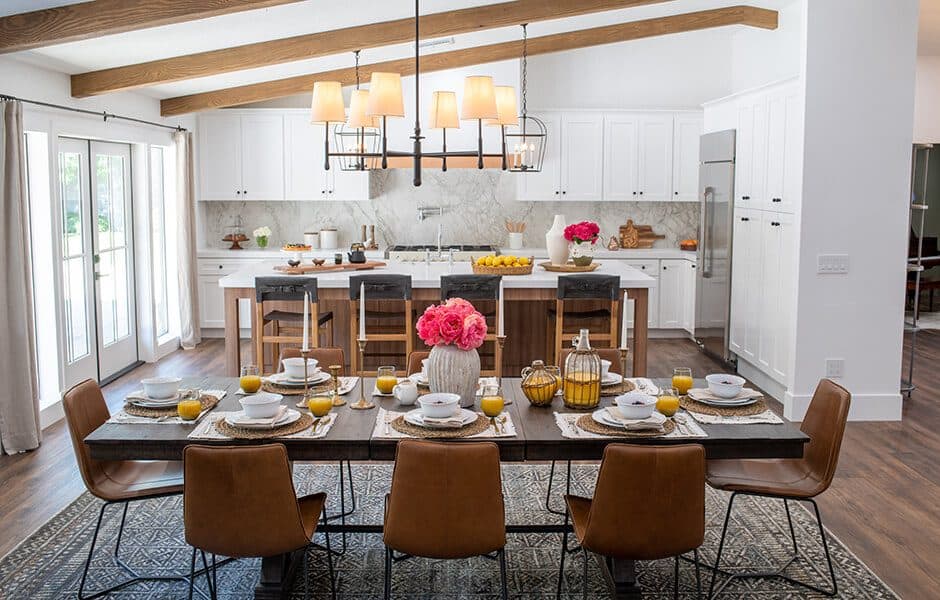 Dining area with a rustic table, leather chairs, and a bright kitchen with white cabinets and wood beams