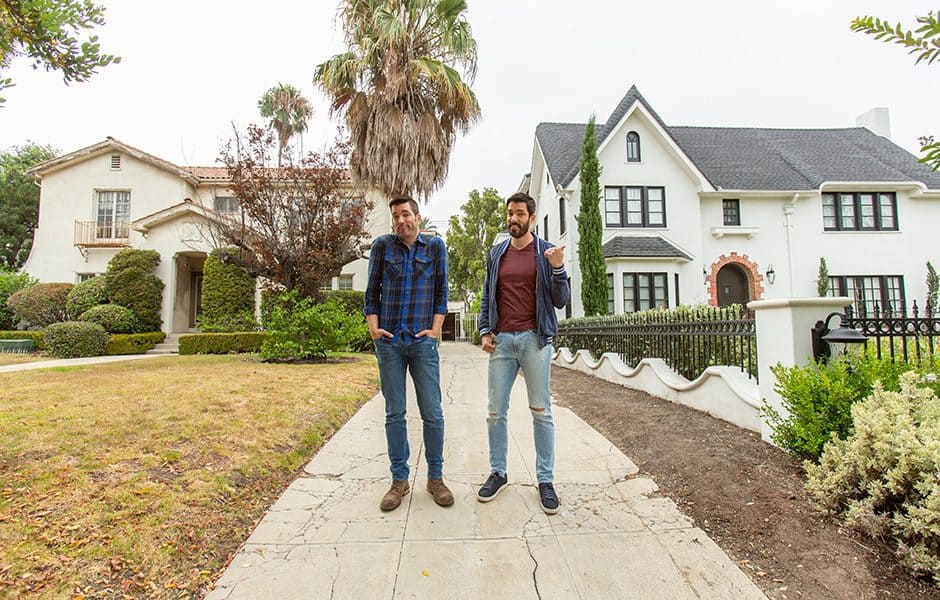 Drew and Jonathan standing on a sidewalk between a traditional beige house and a white Tudor-style home