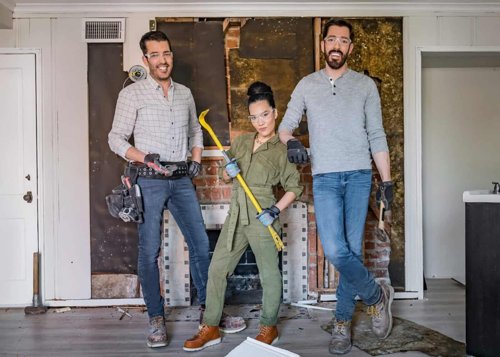 Two men with tools and a woman holding a crowbar in a renovation setting
