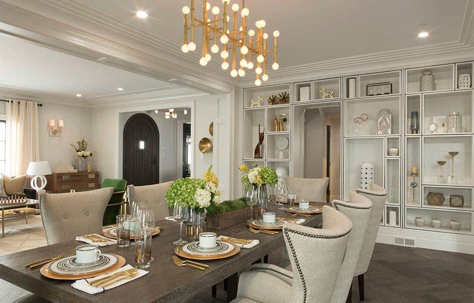 Elegant dining room with a large wooden table, upholstered chairs, decorative shelving, and a modern chandelier