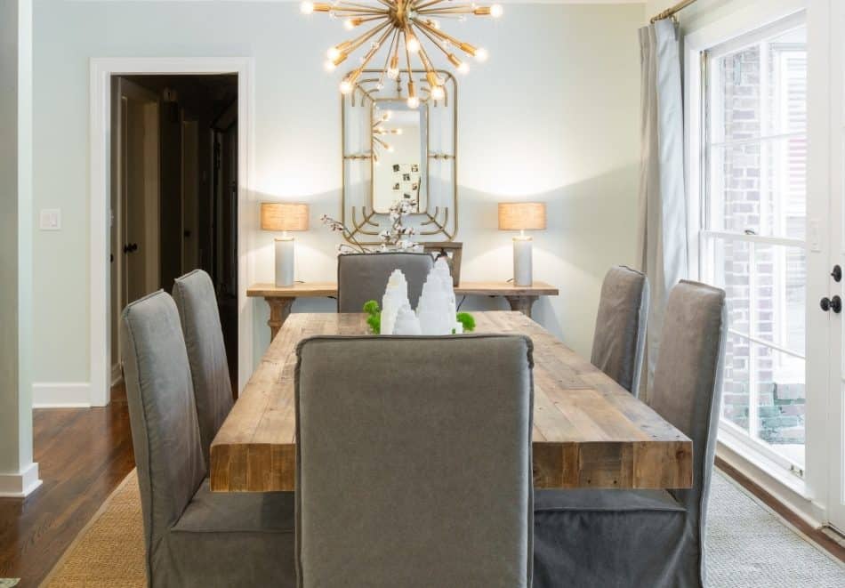 Rustic dining room with a wooden table, gray upholstered chairs, and a modern chandelier