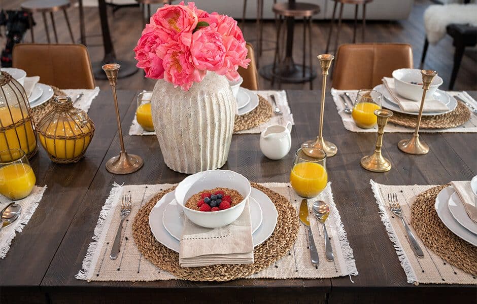 Rustic dining table set with woven placemats, gold accents, and a floral centerpiece