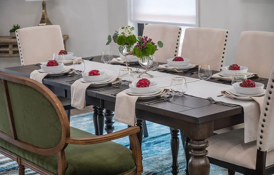 Dining room with dark wooden table, white chairs, patterned rug, table setting with flowers and fruit