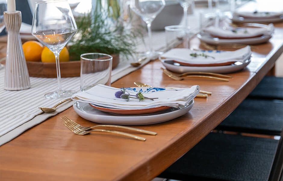 A dining table set for a meal with plates, napkins, silverware, glasses, and a centerpiece of flowers and fruit
