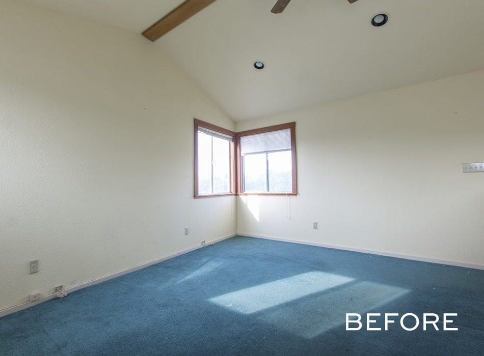 Empty room with beige walls, blue carpet, a vaulted ceiling with wooden beams, and a corner window