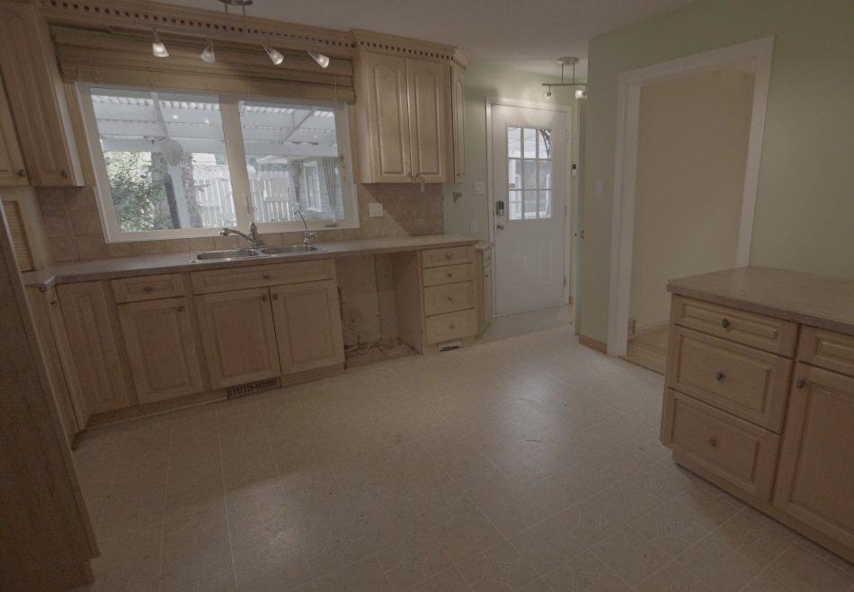 Dated kitchen with wooden cabinets, beige countertops, and a large window overlooking a patio