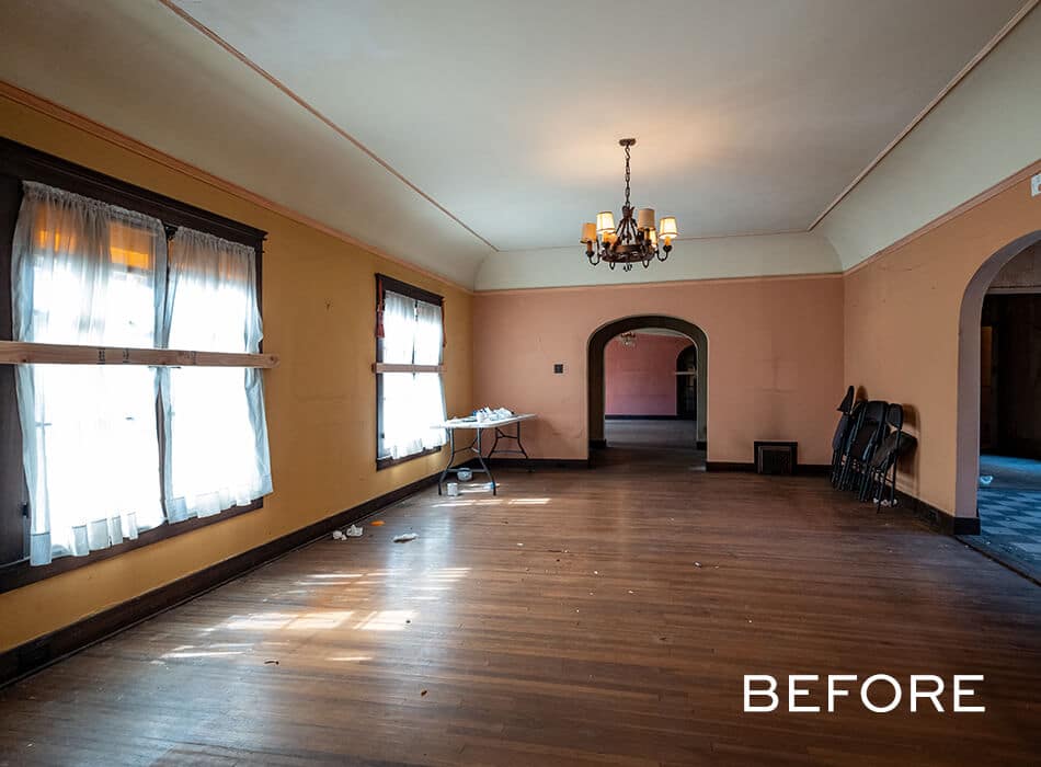 Empty room with peach-colored walls, wood floors, windows with sheer curtains, and a chandelier