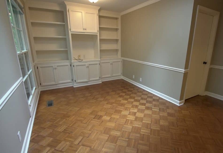 Empty room with built-in white shelving, parquet flooring, and beige walls