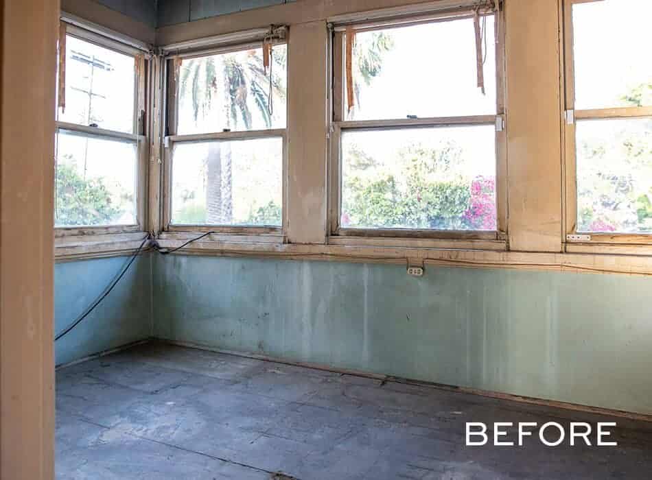 A before image of a small, empty room with painted walls, a wooden floor, and multiple large windows with curtains