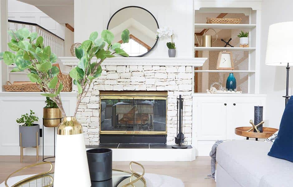 Bright living room with a white stone fireplace, gold accents, and modern décor
