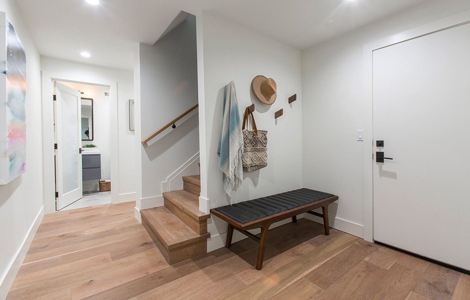Modern entryway with wooden bench, wall hooks, light wood flooring, and staircase