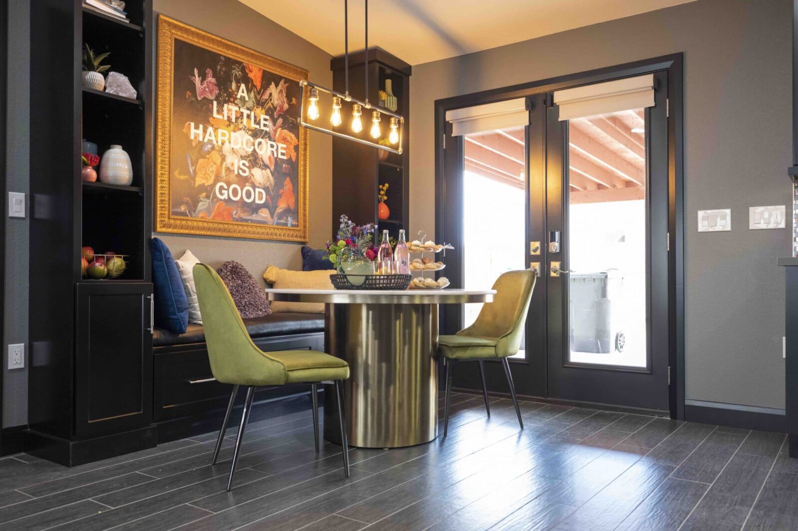 Stylish dining nook with round gold table, green chairs, bench seating, modern lighting, and bold wall art