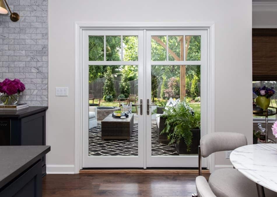 Bright interior view of French doors opening to a cozy outdoor patio with lush greenery and seating