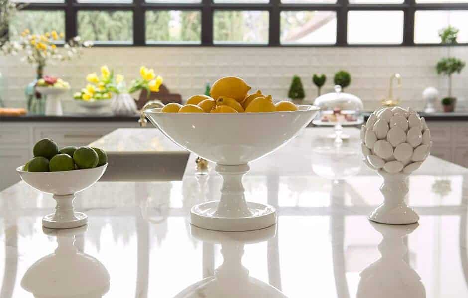 Bright kitchen island with decorative white pedestal bowls holding lemons, limes, and an artichoke-shaped sculpture
