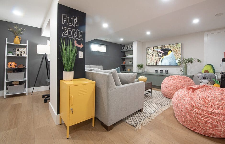 Modern basement playroom with gray sofa, patterned bean bags, wall-mounted TV, and "Fun Zone" sign