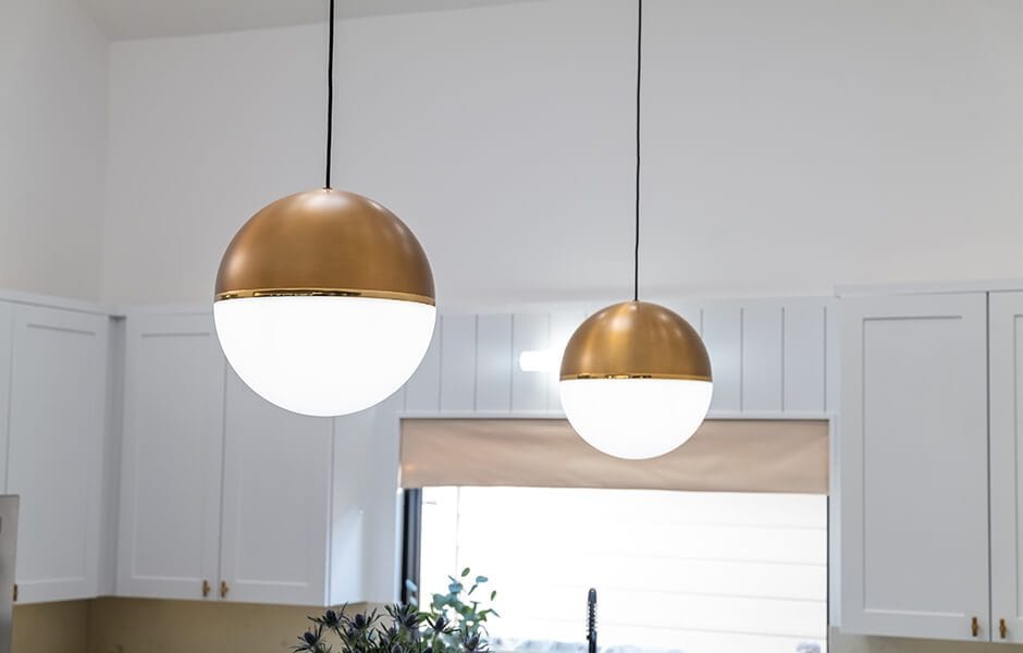 Modern gold and white pendant lights hanging in a bright kitchen with white cabinets
